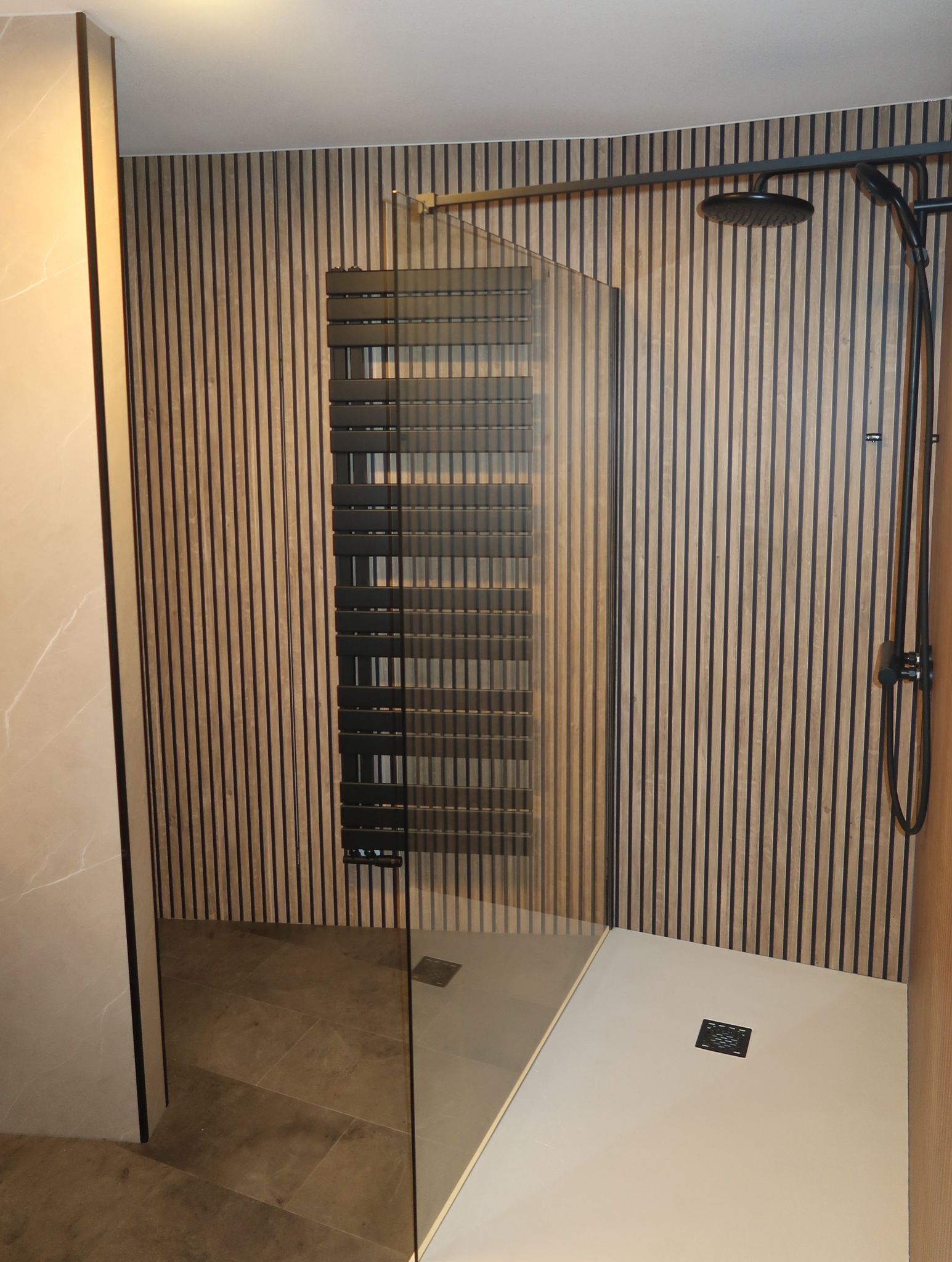 Moderne inloopdouche met houtlook wandpanelen en zwarte handdoekradiator